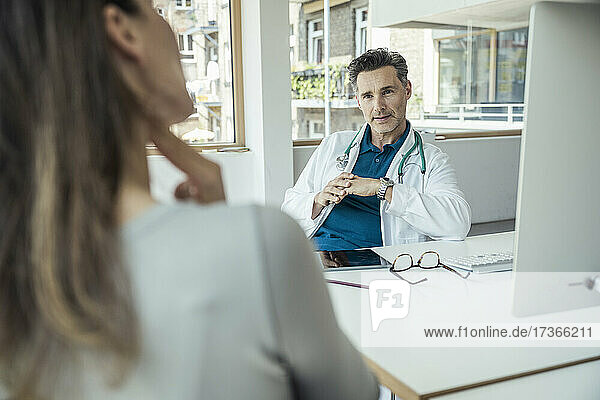 Männlicher Arzt im Gespräch mit einer Patientin im Büro