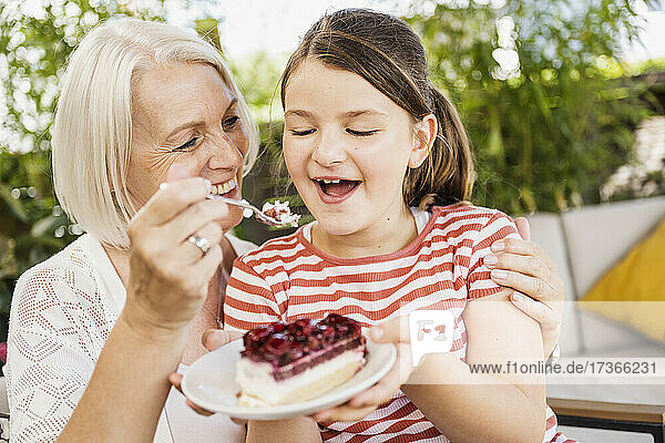 Großmutter füttert ihre Enkelin auf dem Balkon mit Kuchen