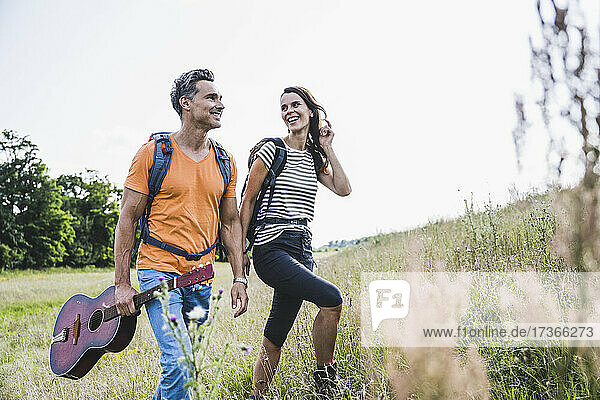 Lächelnde Frau schaut auf Mann mit Gitarre beim Wandern