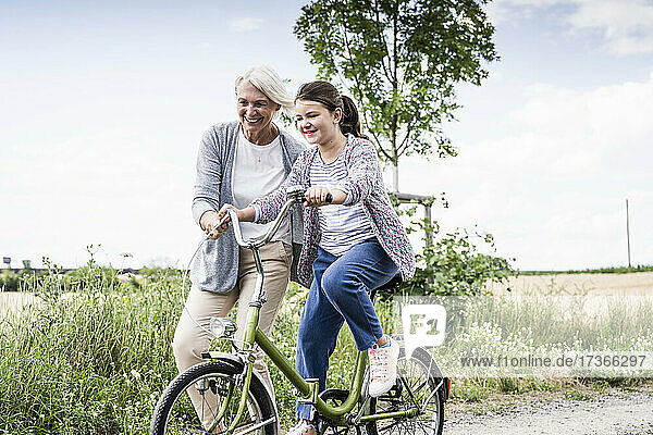 Smiling woman teaching girl riding bicycle on dirt road