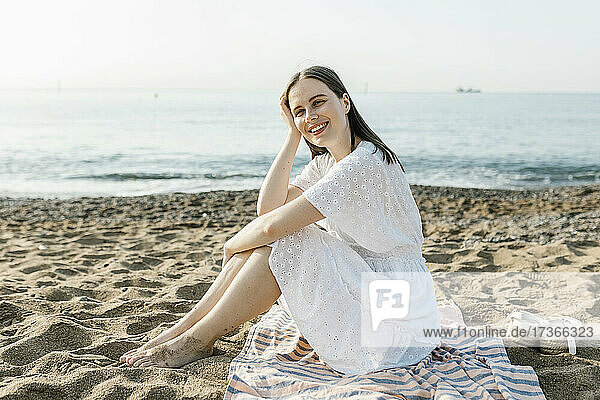 Glückliche schöne Frau sitzt auf Strandtuch