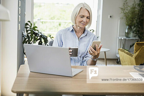 Reife weibliche Berufstätige  die ein Smartphone am Schreibtisch im Home Office benutzt