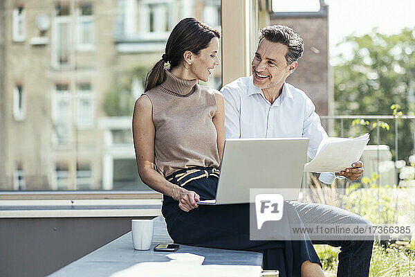 Businesswoman having discussion with colleague while sitting on retaining wall