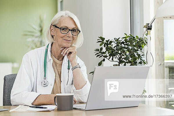 Smiling female doctor with hand on chin at desk