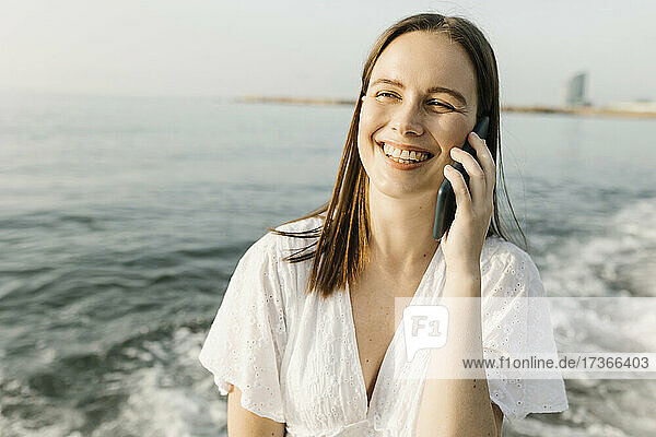 Glückliche Frau  die am Strand mit einem Mobiltelefon spricht