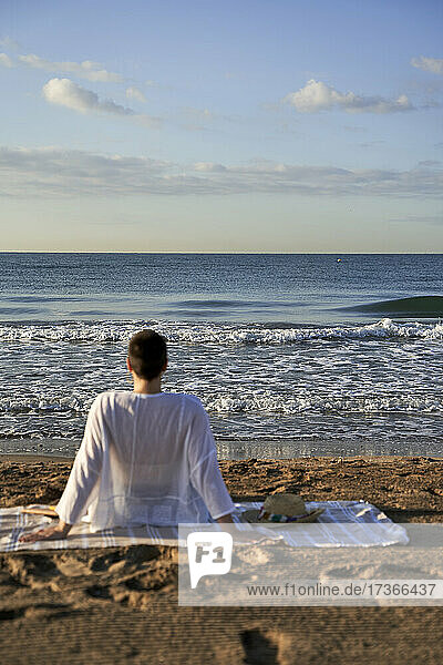 Frau schaut auf das Meer  während sie auf einer Decke sitzt