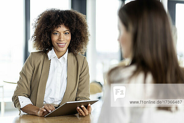 Lächelnde Geschäftsfrau  die ein digitales Tablet hält  während sie mit einem Kollegen im Büro steht