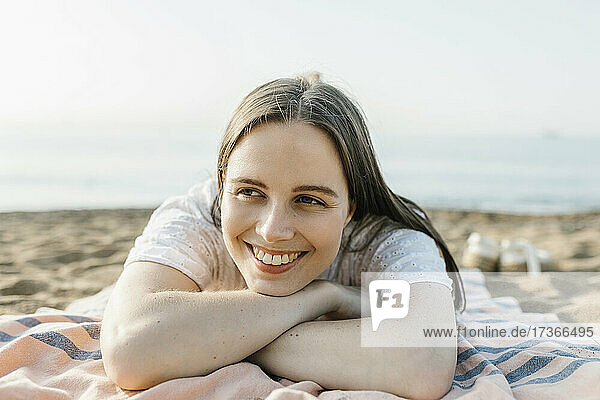 Smiling woman relaxing while lying on beach towel