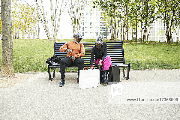 Frau kontrolliert Einkaufstaschen  während sie mit einem Mann auf einer Bank sitzt