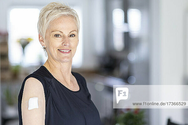 Mature woman with bandage on shoulder after vaccination at home