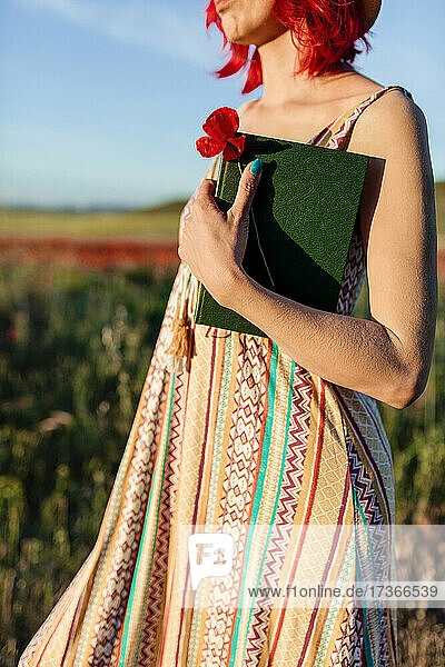Frau hält Mohnblume und Buch auf einem Feld