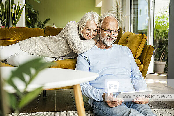 Woman leaning on shoulders of man using digital tablet at home