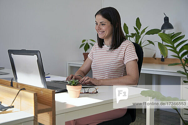 Lächelnde weibliche Fachkraft  die im Büro einen Laptop benutzt