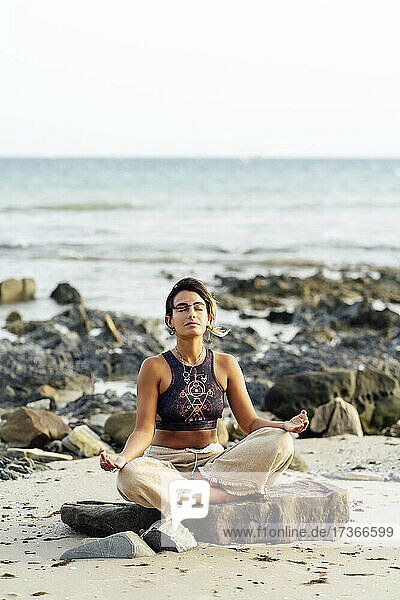 Junge Frau übt Yoga auf einem Felsen am Strand