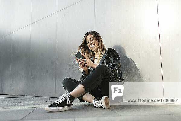 Lächelnde Frau mit Smartphone vor einer silbernen Wand