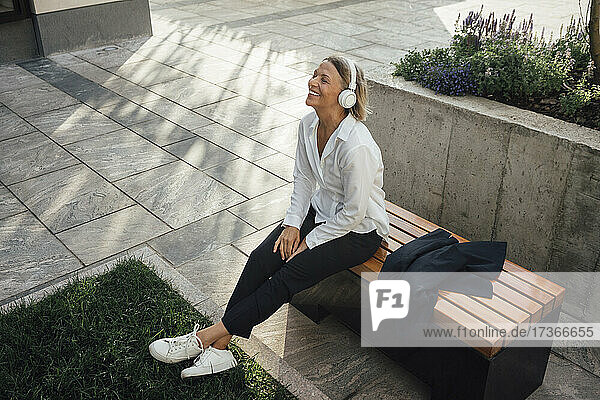 Lächelnde Geschäftsfrau  die auf einer Bank sitzend Musik hört
