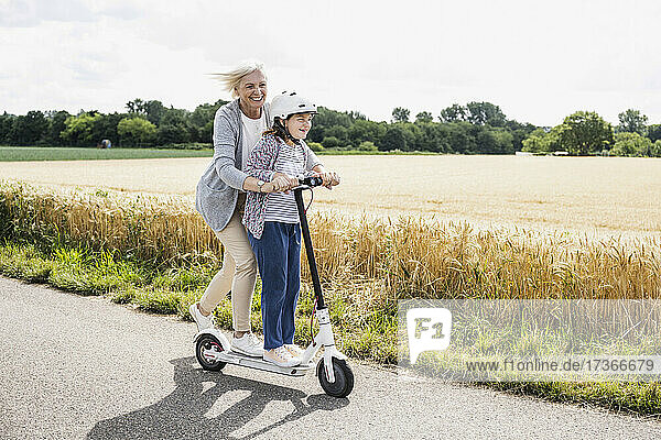 Glückliche Enkelin und Großmutter spielen beim Fahren mit dem Roller an einem sonnigen Tag