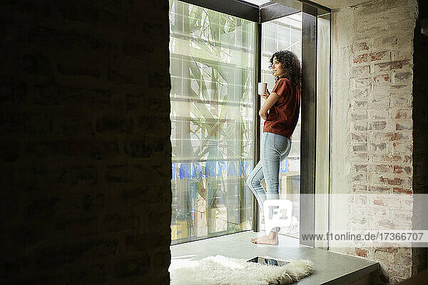 Businesswoman holding coffee cup while looking through window