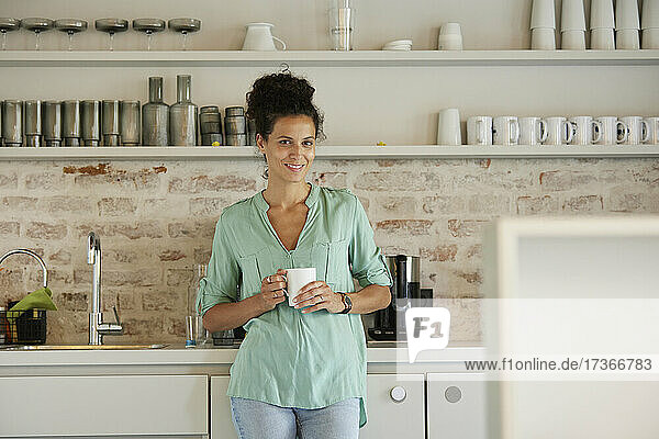 Smiling businesswoman holding coffee cup while standing at cafeteria