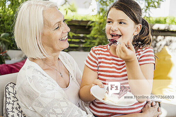 Enkelin isst Kuchen  während sie mit ihrer Großmutter auf dem Balkon sitzt