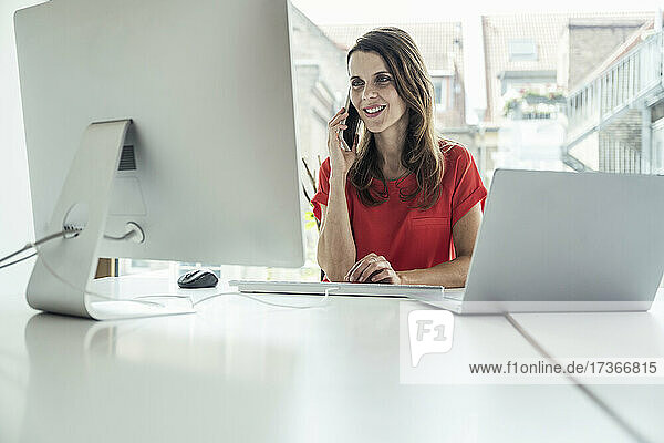 Geschäftsfrau  die mit einem Mobiltelefon spricht  während sie einen Computer im Büro benutzt