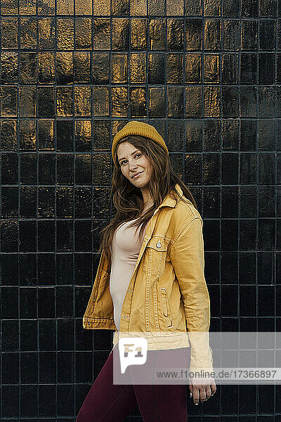 Junge Frau mit gelber Strickmütze und Jacke vor einer schwarzen Wand