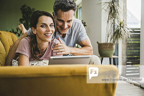 Smiling couple using digital tablet on sofa at home