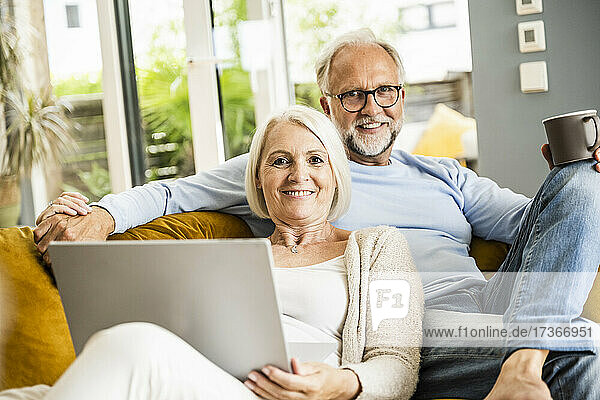 Woman with laptop holding hand of man while sitting on sofa