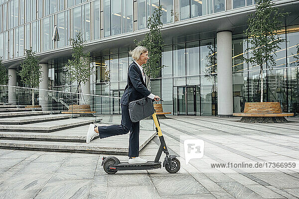 Businesswoman riding electric push scooter in office park