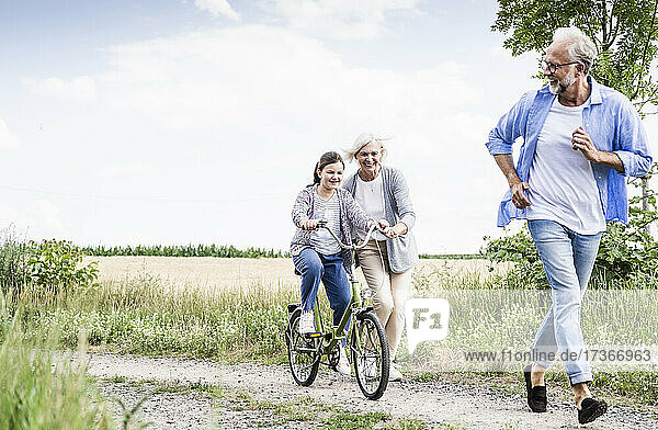 Girl riding bicycle with woman behind man on dirt road
