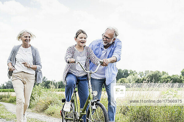 Mann bringt Mädchen das Fahrradfahren bei  während die Frau auf dem Feldweg hinterherläuft