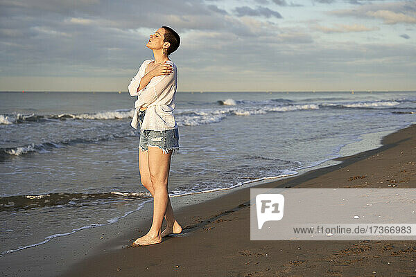 Junge Frau umarmt sich selbst  während sie am Strand steht