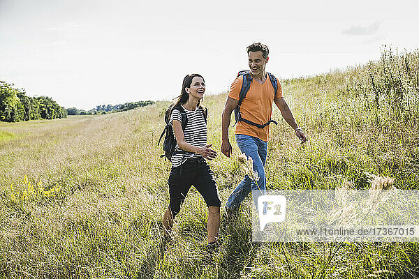 Lächelndes Paar mit Rucksäcken wandern zusammen auf Gras während sonnigen Tag