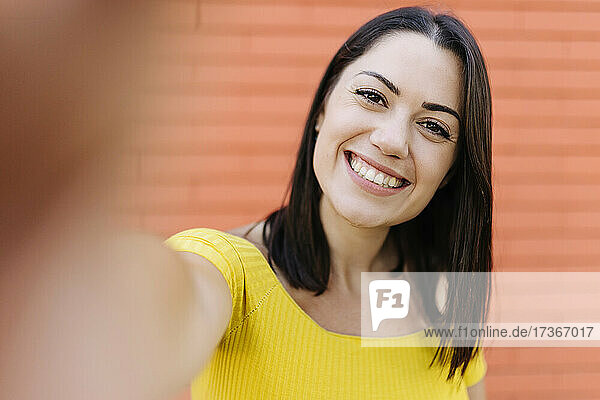 Lächelnde junge Frau  die ein Selfie vor einer Wand macht