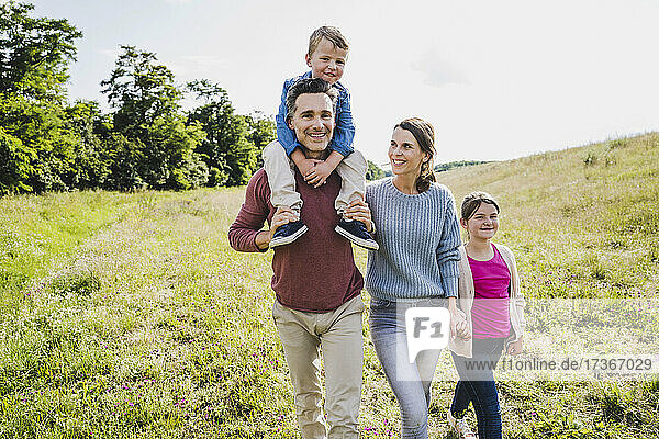 Vater trägt seinen Sohn auf den Schultern beim Spaziergang mit der Familie auf einer Wiese