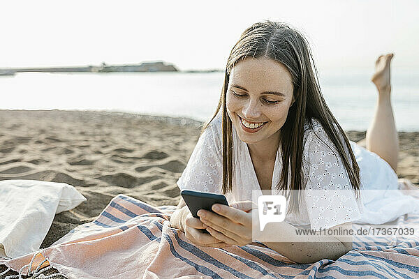 Junge Frau benutzt ein Mobiltelefon  während sie auf einem Strandtuch liegt