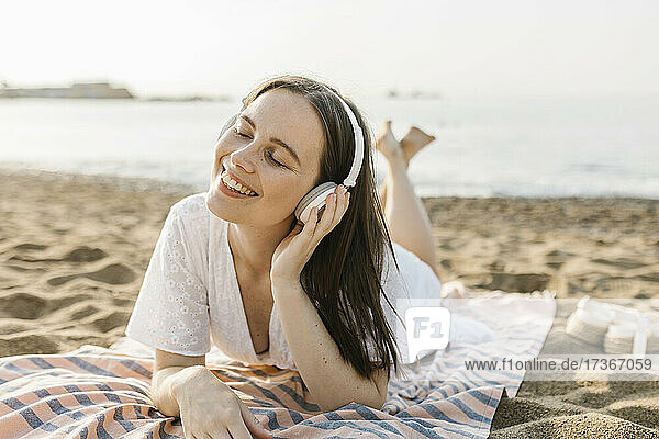 Smiling woman listening music through headphones while lying on towel