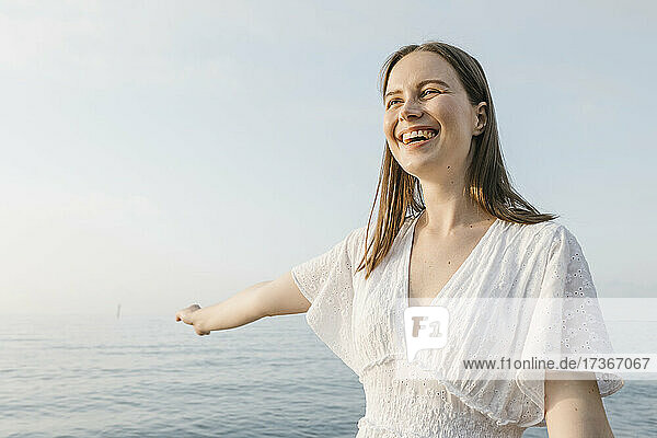 Schöne junge Frau  die lachend mit ausgestrecktem Arm am Strand steht