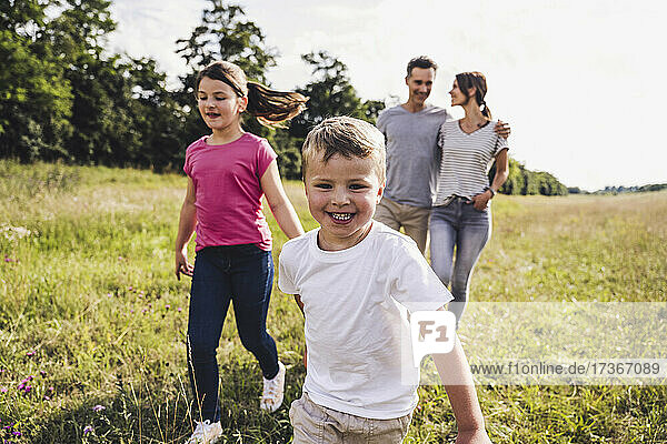 Boy with sister running while parents walking on meadow