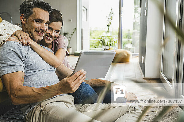 Frau umarmt Mann mit digitalem Tablet zu Hause