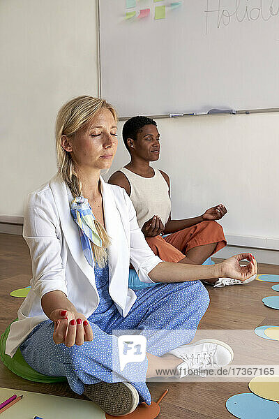 Businesswoman doing yoga with colleague in office