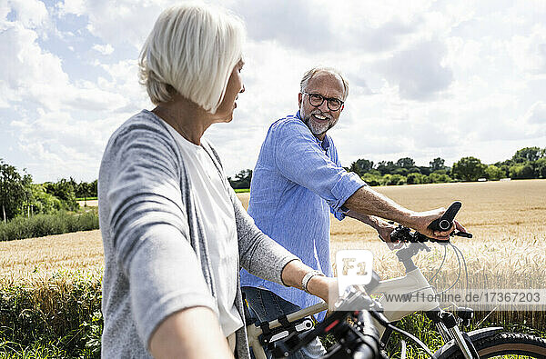 Mann im Gespräch mit Frau beim Spaziergang mit Fahrrad an einem sonnigen Tag