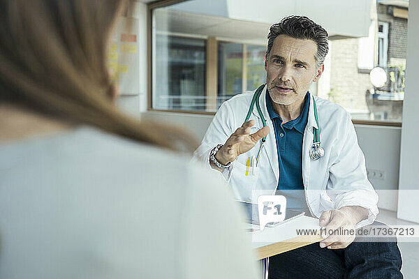 Männlicher Arzt erklärt Patientin im Sitzen im Büro