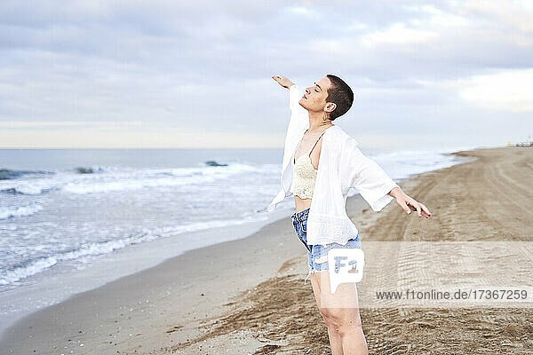 Carefree woman with arms outstretched standing at beach