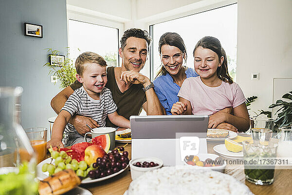Familie betrachtet digitales Tablet auf dem Tisch  während sie zu Hause frühstücken