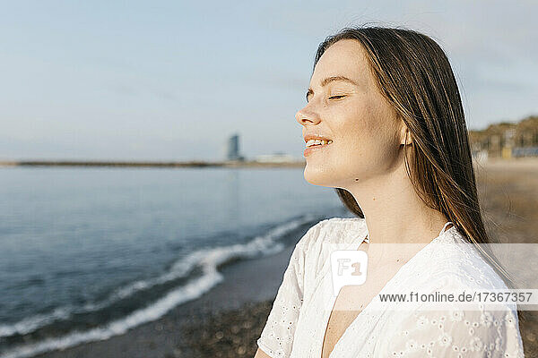 Lächelnde junge Frau mit geschlossenen Augen am Strand