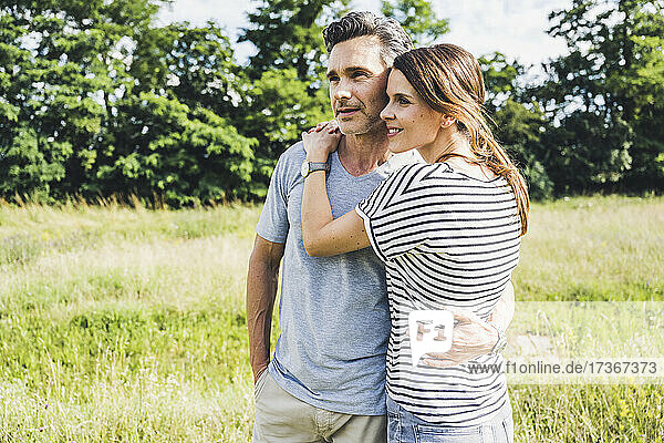 Woman embracing man while standing on grass during sunny day