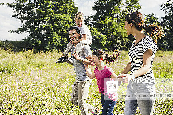 Glückliche Familie  die sich an den Händen hält  während sie an einem sonnigen Tag im Gras läuft