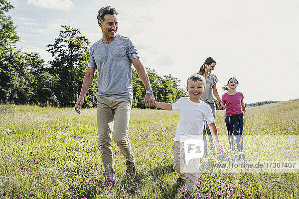 Parents holding hands of children while walking on grass