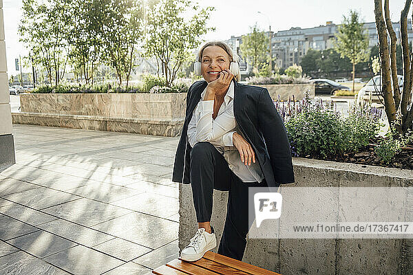 Female professional listening music while leaning on bench
